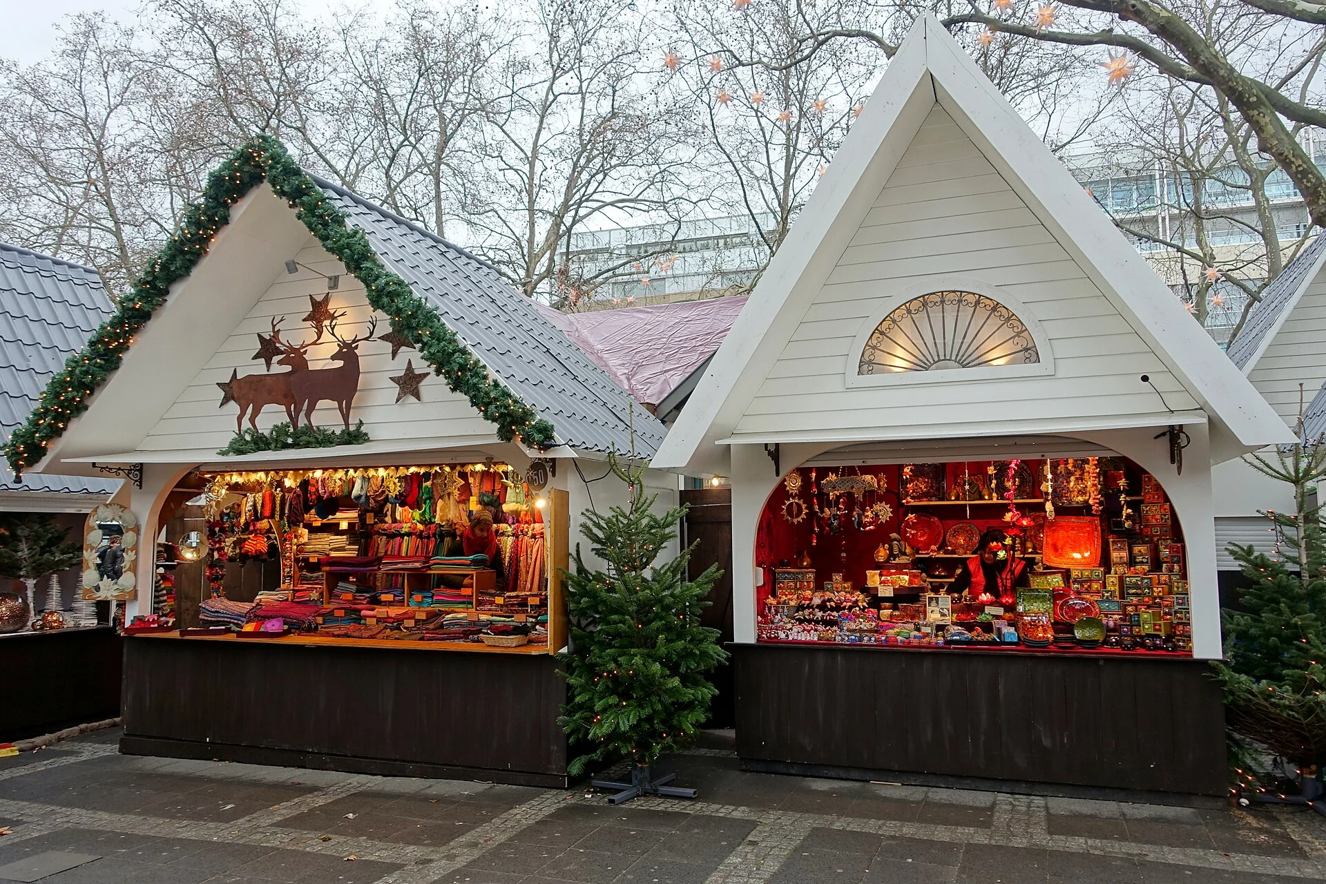 Wooden Christmas market stalls decorated with evergreen garland and red trim, filled with holiday goods.